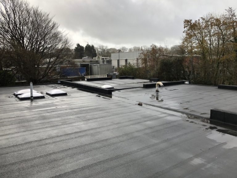 View over flat roofing finished with water proofing layer with trees and buildings in the background